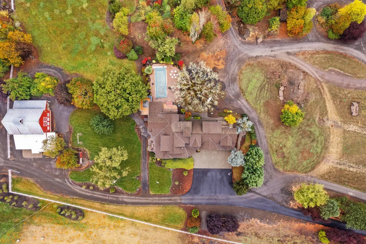 A wide-angle exterior view of the main Roloff Family farmhouse set amidst landscaped gardens, a swimming pool, and mature surrounding trees. The property glows under the soft light of sunset, with inviting outdoor spaces perfect for gatherings, relaxation, or simply taking in the serene scenery.