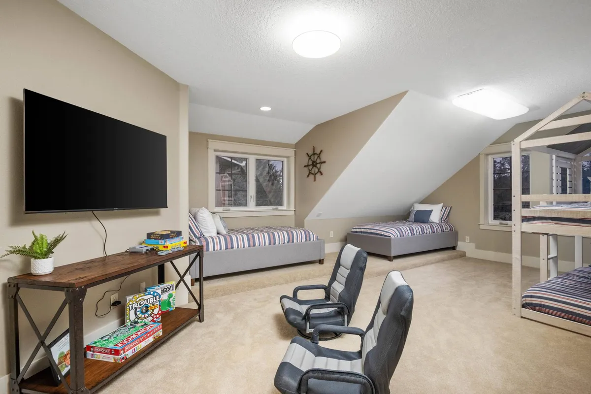A cheerful bunk room featuring a sturdy bunk bed, striped bedding, a television, and a wooden shelf stocked with games. The space is bright and inviting—perfect for families or children seeking fun and private quarters.