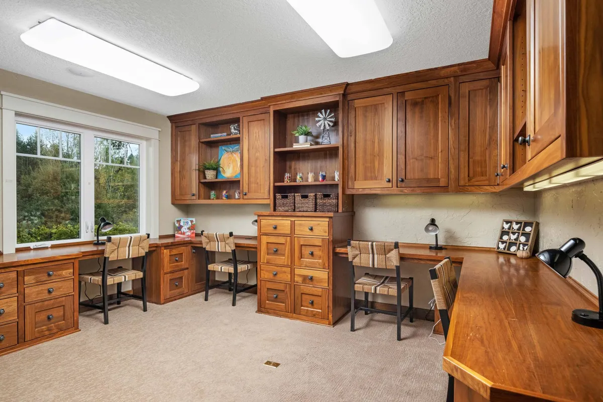 A workspace with wooden cabinetry, multiple workstations by a bright window, and creative supplies, ideal for focused solo work, small meetings, or brainstorming sessions. The atmosphere is bright and conducive to productivity.
