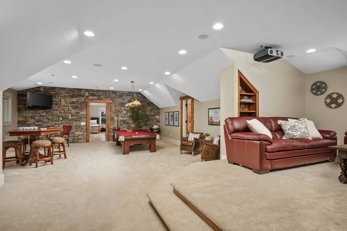 This inviting interior scene showcases a pool table, leather sofa, dining table, and a projector screen, all set against a cozy stone accent wall. The space is perfect for movie nights, parties, or relaxing after a day of activities.