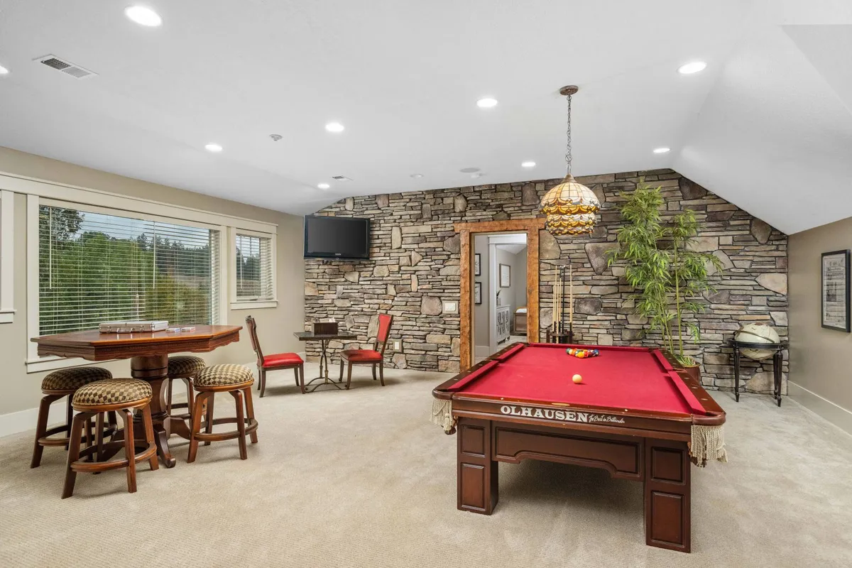 A stylish great room anchored by a pool table, bar table, and stone wall, illuminated by a hanging lamp. The casual ambiance and layout make it perfect for billiards, socializing, or watching TV.