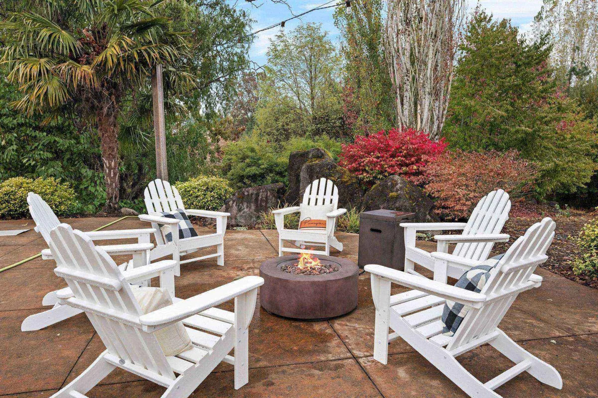 A cozy fire pit area with Adirondack chairs nestled among vibrant greenery. The setting is perfect for evening gatherings, storytelling, or roasting s’mores under the stars, with a welcoming and communal atmosphere.