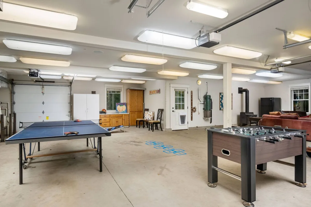This image displays a lively converted garage game room, featuring a ping pong table and a foosball table, with a comfortable seating area and a large garage door that lets in natural light. The casual setup and open space invite friendly competition and relaxed gatherings.