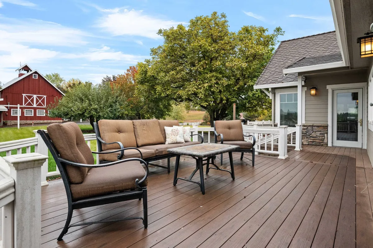A serene outdoor seating area with cushioned chairs and a table, set against the backdrop of a classic red barn and vibrant greenery. The space is ideal for morning coffee, evening drinks, or casual gatherings, all while immersing guests in the farm's rural charm.