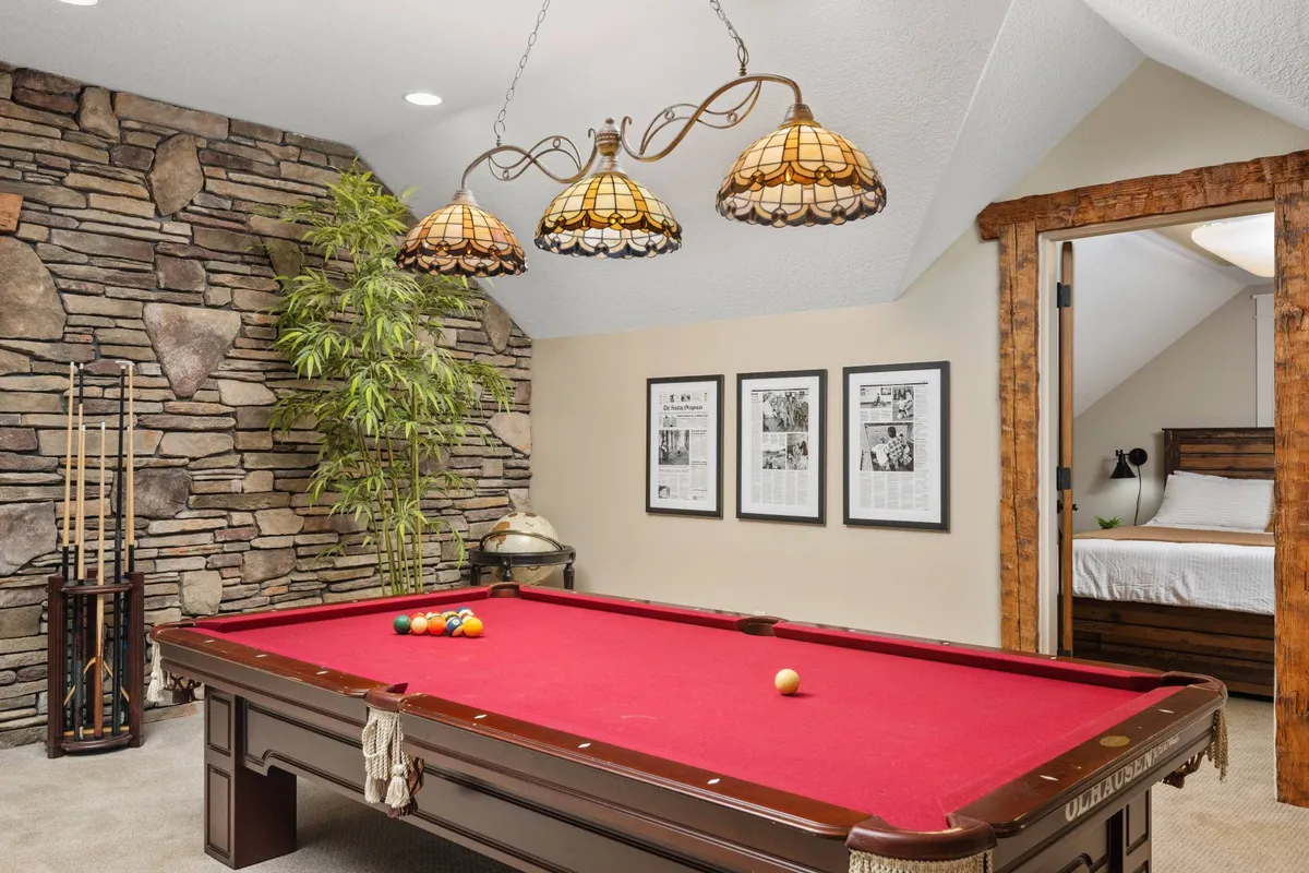 This image highlights a stylish upstairs game room featuring a pool table, stone wall accents, hanging lamps, and framed pictures, creating a space for entertainment and relaxation with friends or family.