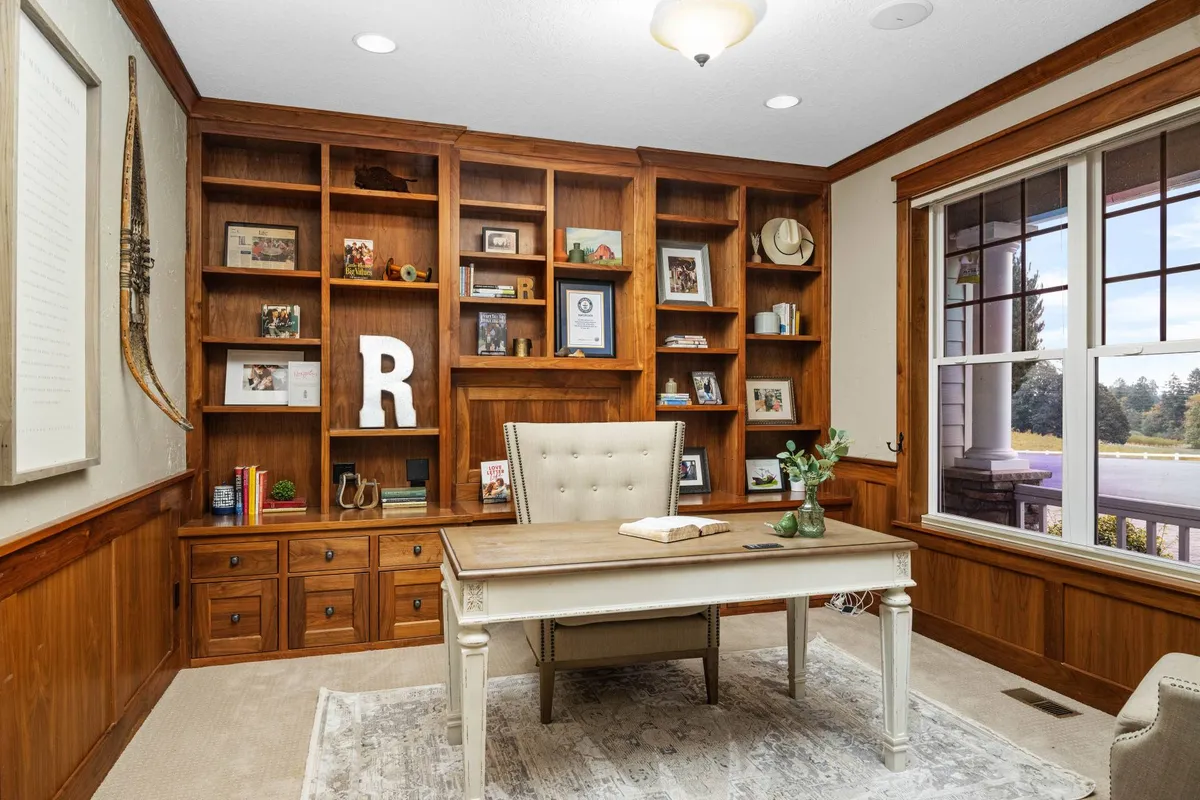 A cozy upstairs sitting area with a wooden bookshelf, an executive desk, a comfortable chair, and decorative items. The space is bathed in natural light from large windows, inviting quiet moments of reading or reflection.