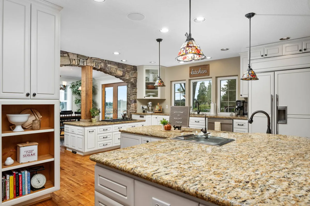The fully stocked kitchen features a granite-topped island, stylish stained glass pendant lights, and a dramatic stone archway. The layout is accessible, designed to accommodate cooks of all ages and abilities.