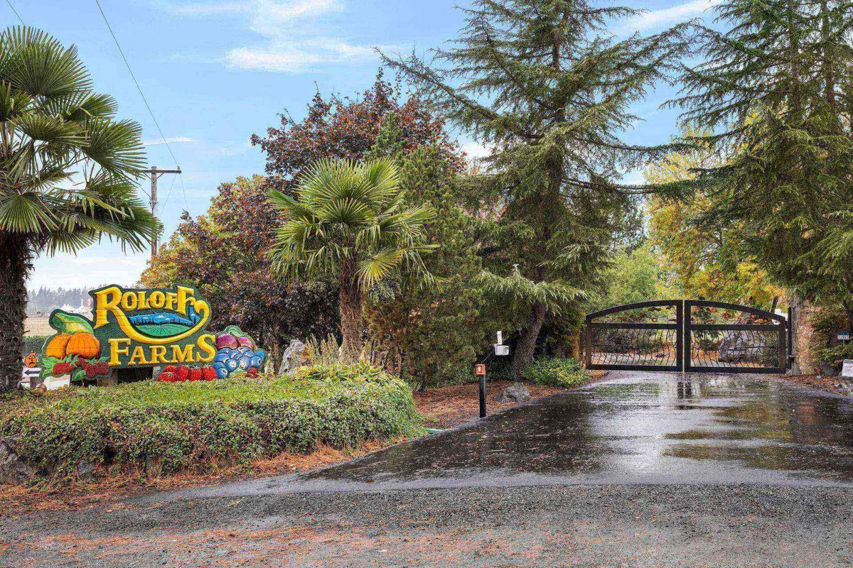 A colorful farm sign marks the gated entrance, surrounded by lush greenery, welcoming guests to the property. The gated entry ensures privacy and security while hinting at festive seasonal events like harvest festivals and pumpkin picking.